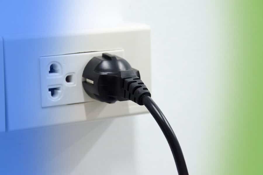 A black power plug with an attached cable is inserted into a white electrical wall outlet.